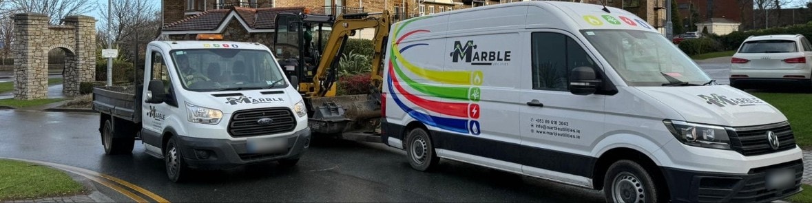 A Marble tipper truck, mini excavator and liveried crew van parked on a residential street.