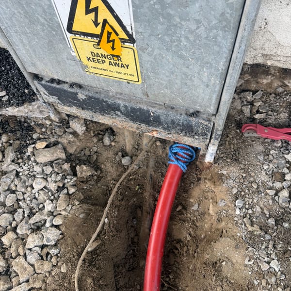 A red electricity duct with a draw rope entering the base of a feeder pillar marked "Danger, keep away".