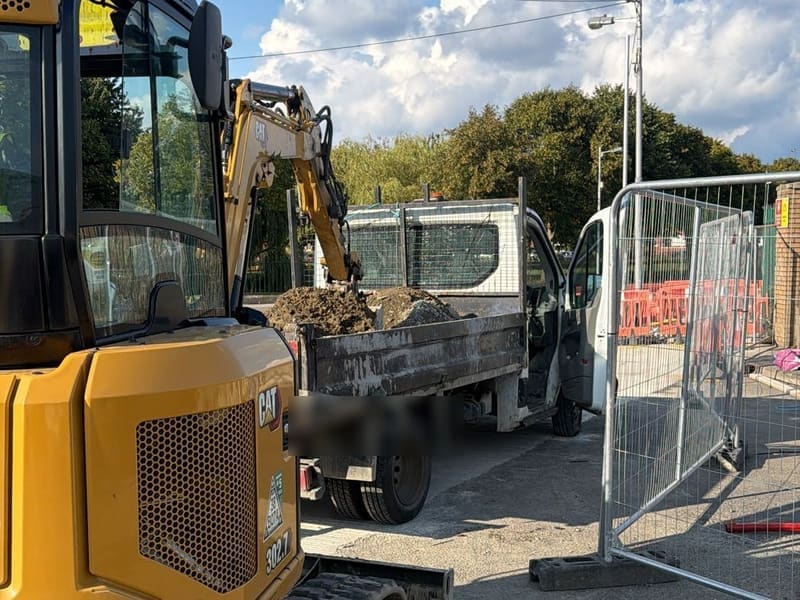 A Marble CAT mini excavator loading spoil into a tipper inside fenced works.
