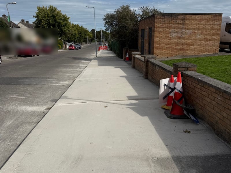A long run of new concrete footway beside a road on a sunny day.