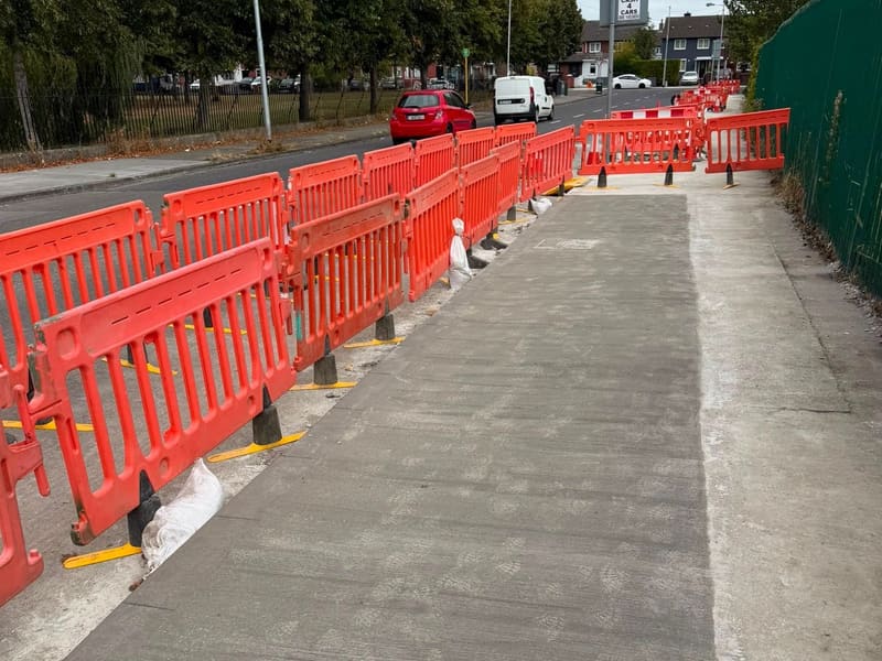 A long run of new concrete footway behind pedestrian barriers.