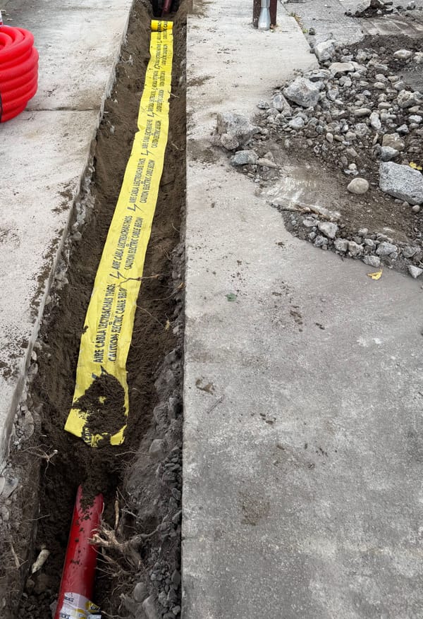 A footway trench with yellow cable warning tape laid over the backfill and red duct visible at the end.