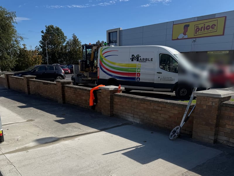 A Marble Utilities liveried van parked behind a newly finished concrete footpath beside a retail park.